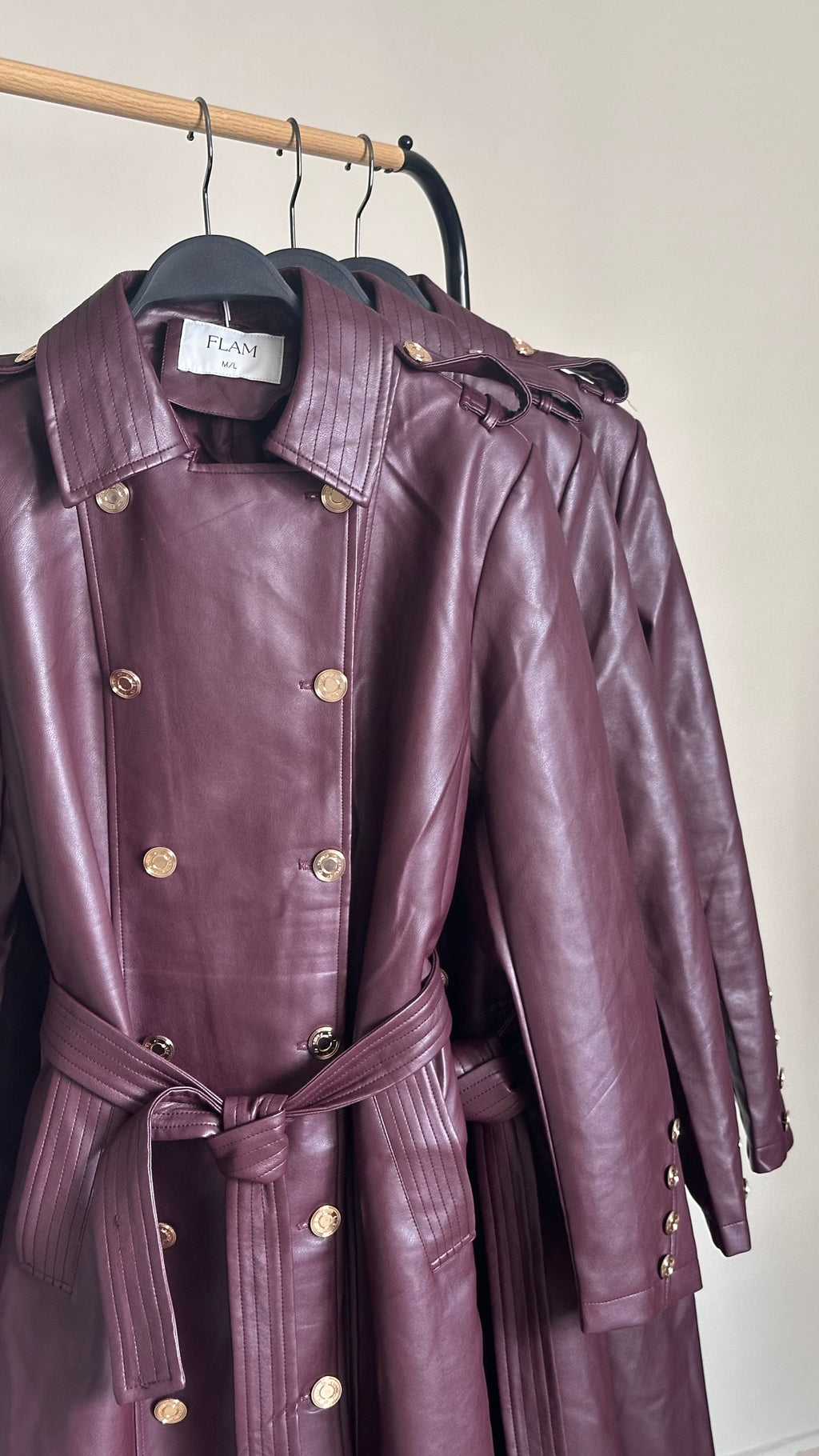 A burgundy faux-leather trench coat with gold-tone buttons and a matching waist tie.